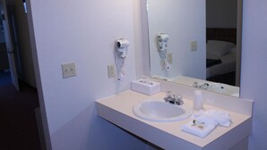 A hotel bathroom with a white sink, a mirror, and a hairdryer mounted on the wall.