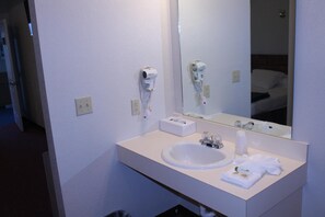 A hotel bathroom with a white sink, a mirror, and a hairdryer mounted on the wall.