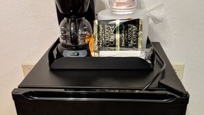 Uma geladeira Haier preta com um preparador de café e um dosador de cápsulas de café em cima.