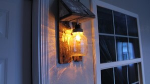 A rustic wall-mounted light fixture with a mason jar design, mounted on a wooden board against a wall.