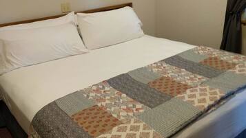 A single bed with white linens and a patchwork quilt.