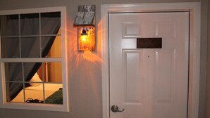 Um quarto com janela, porta e luminária fixada na parede.