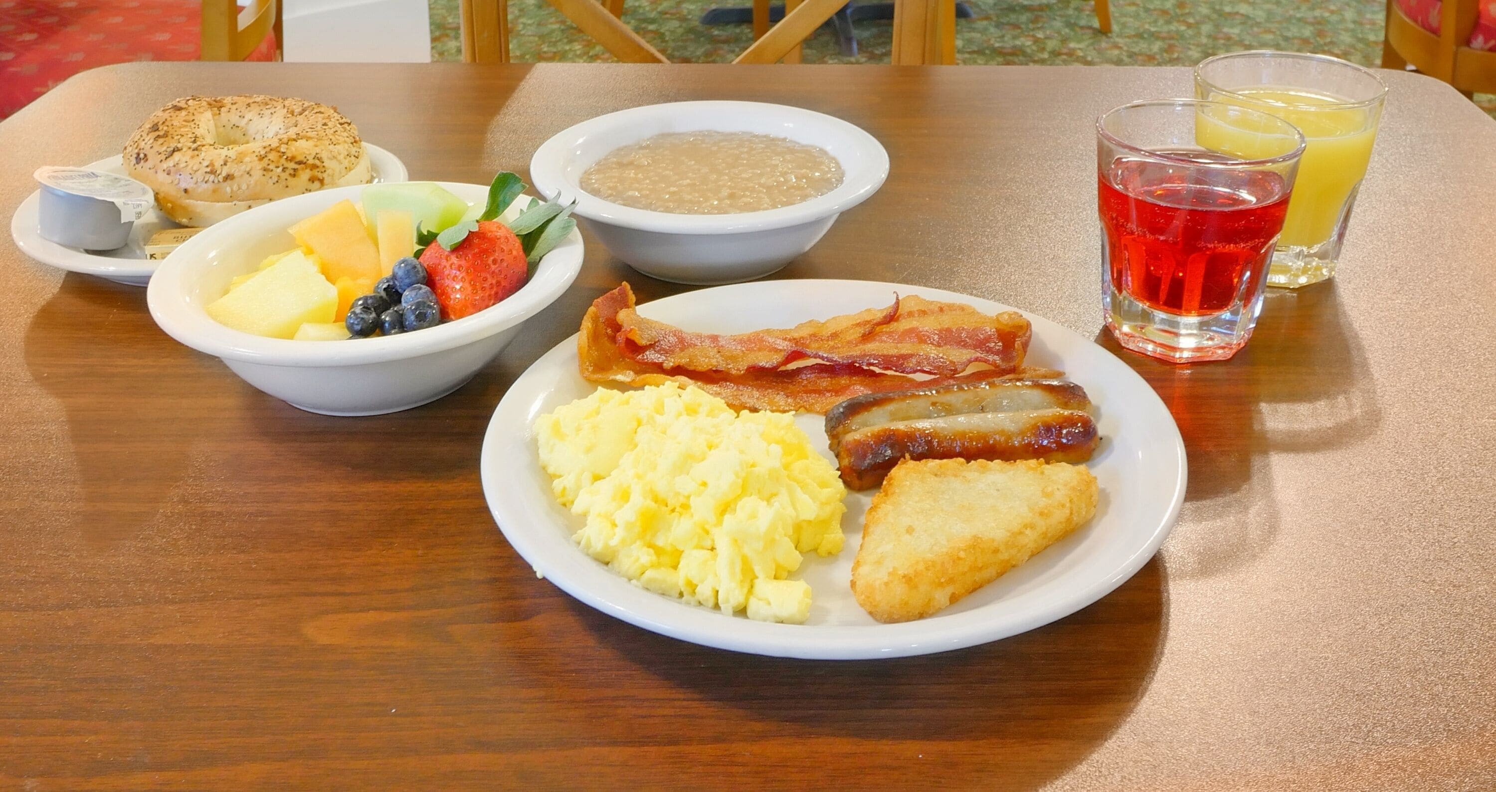 A breakfast plate with scrambled eggs, bacon, sausage, toast, and fruit.