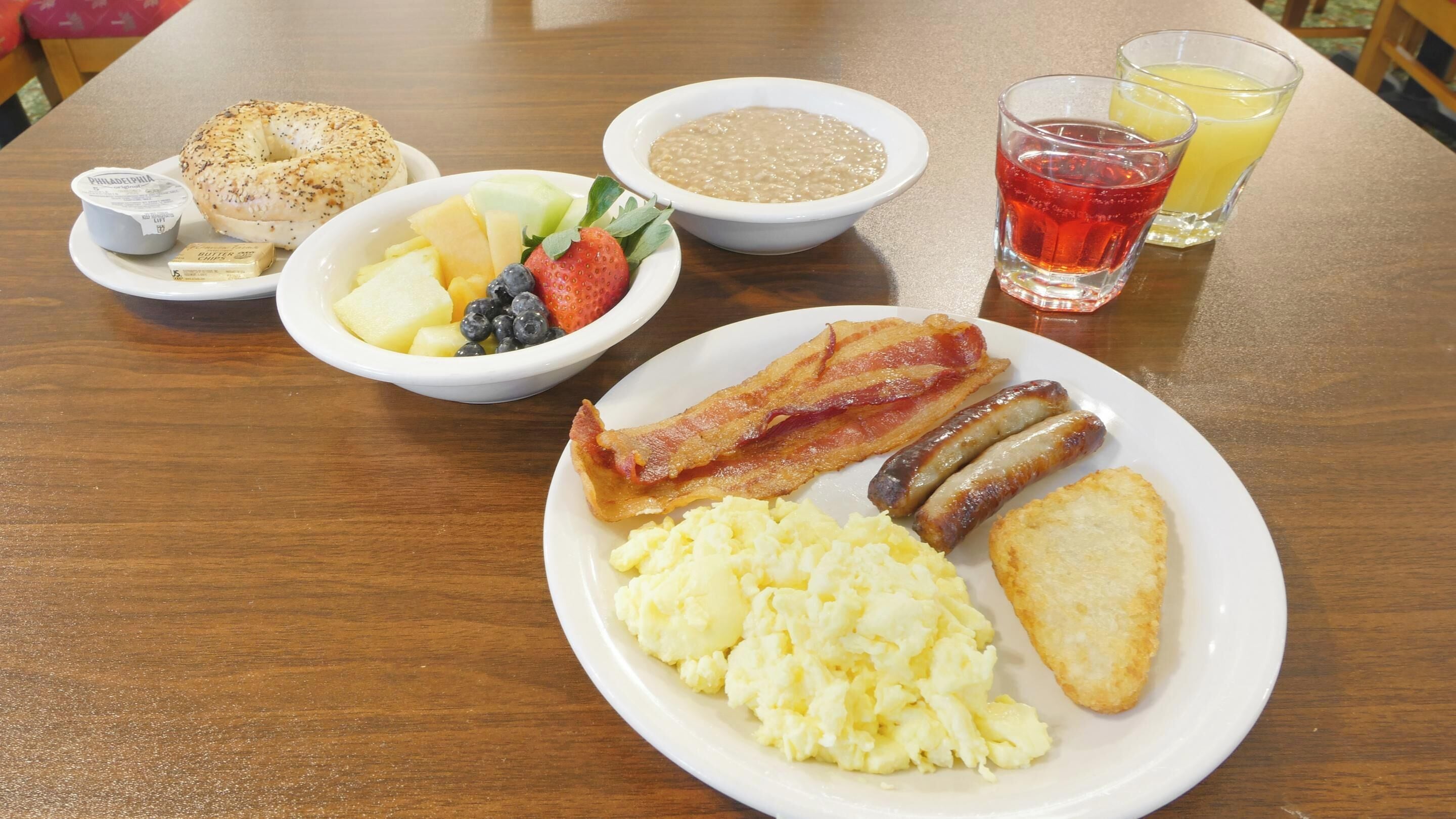 Um prato de café da manhã com ovos, bacon, salsichas, torradas e uma tigela de frutas.