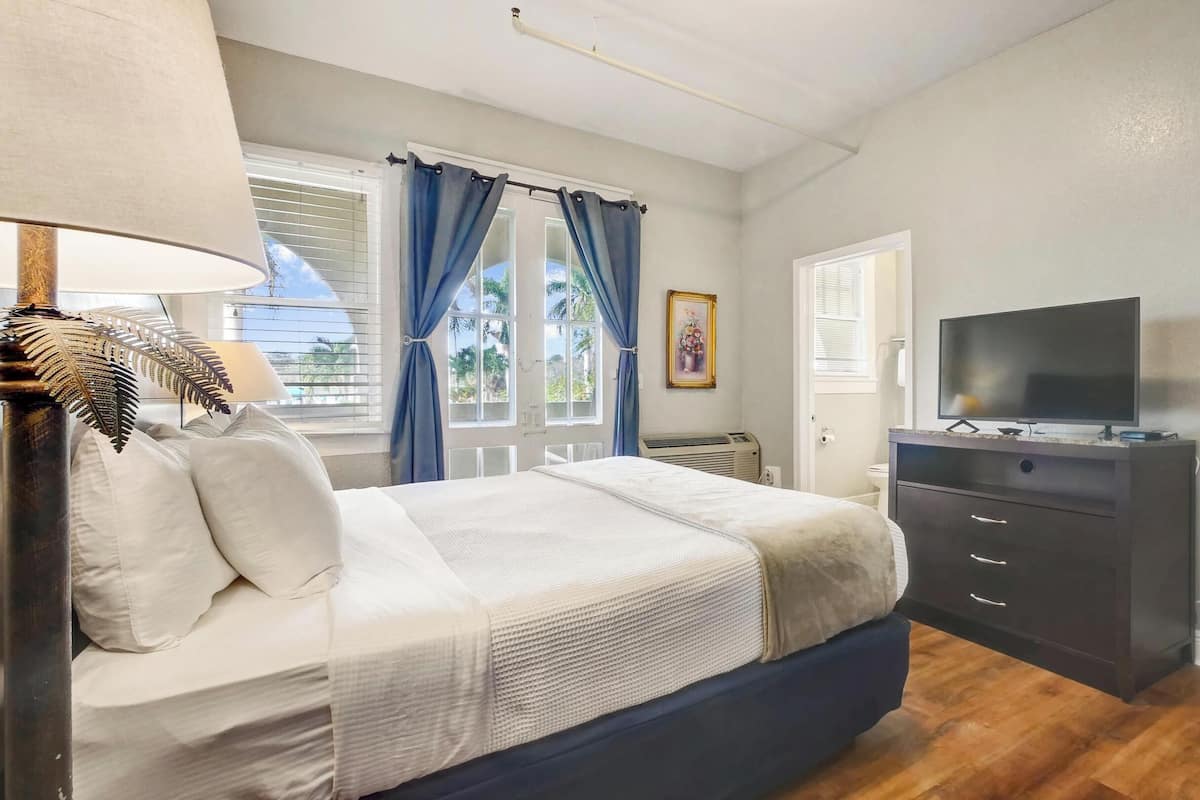 Une chambre à coucher avec un lit, une commode, une télévision et une fenêtre avec des rideaux.