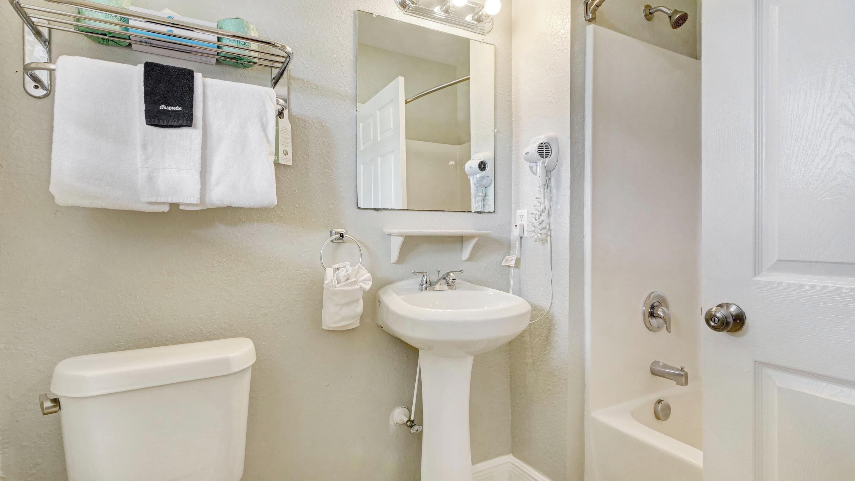 Une salle de bain équipée d’un WC, d’un lavabo et d’une douche. On y trouve également un porte-serviettes avec des serviettes et un sèche-cheveux.