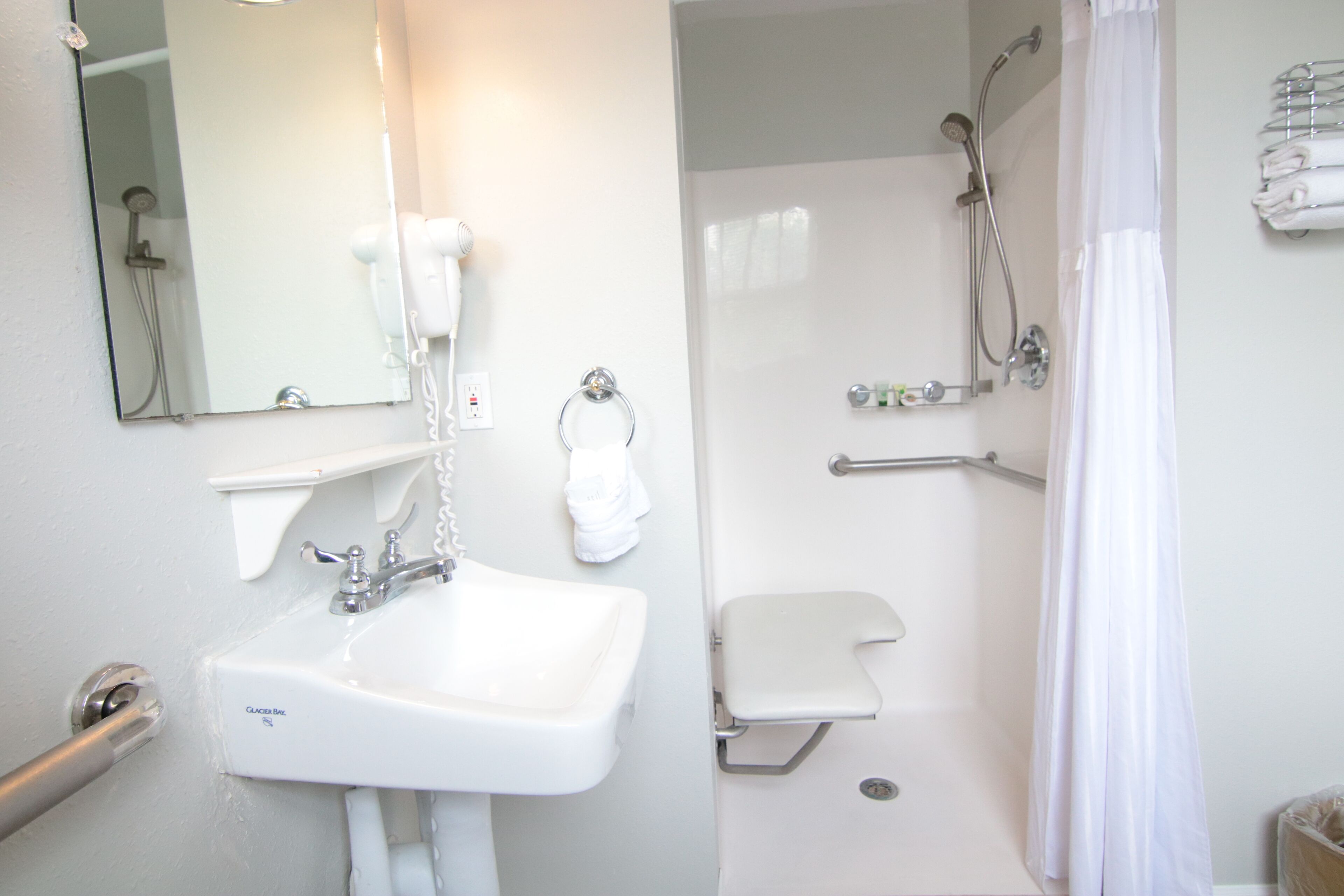 A bathroom with a sink, mirror, towel rack, shower, and toilet.