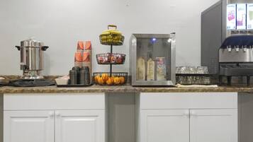 Una encimera de cocina con una cafetera, platos apilados, una cesta de frutas, un cartón de leche y un dispensador de agua.