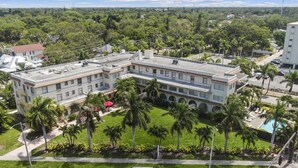 Un grand immeuble à plusieurs étages, doté d’un toit plat, entouré d’une végétation luxuriante et de palmiers.