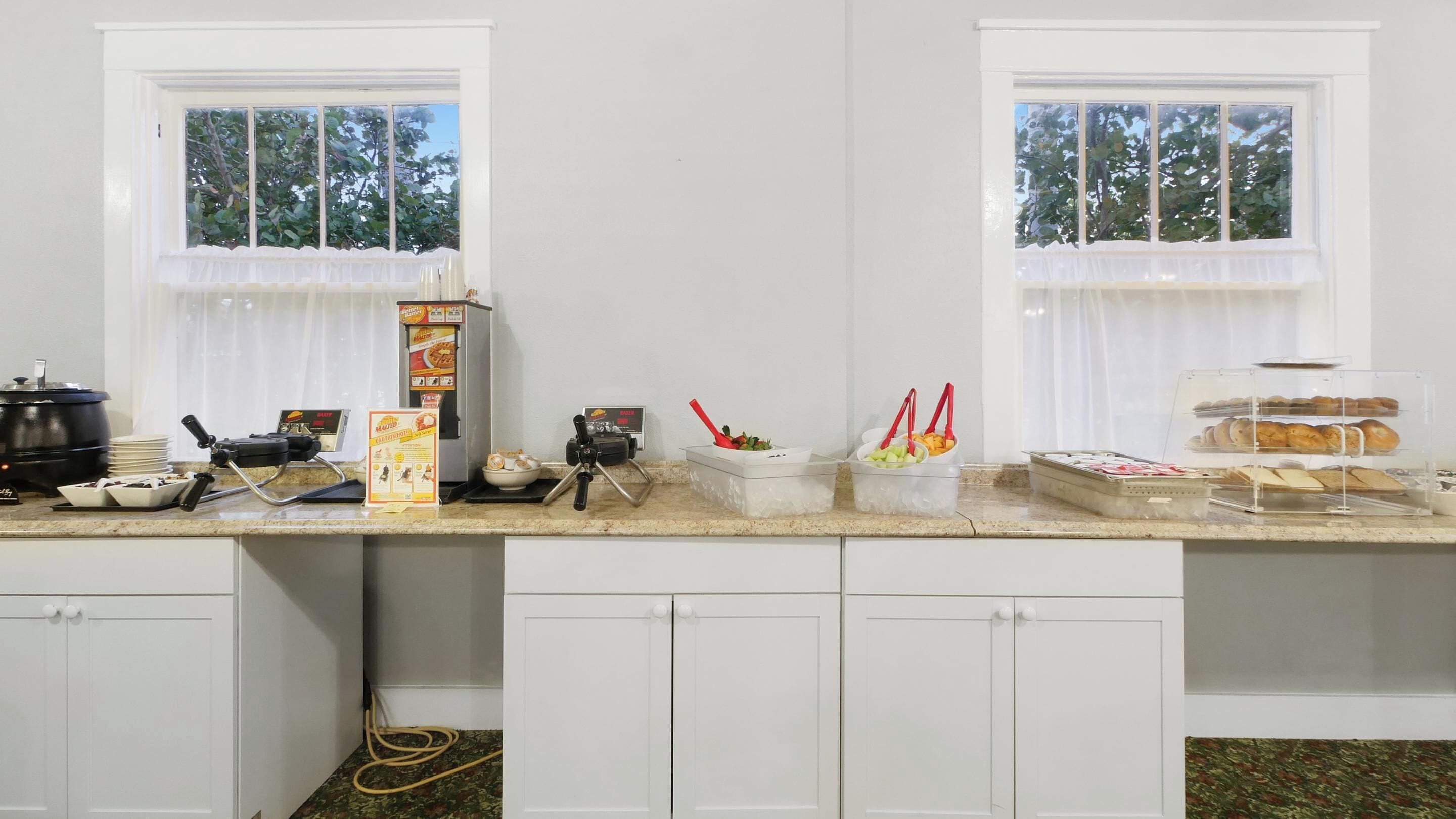 A kitchen with two windows, a coffee machine, a bread display, and a kettle.