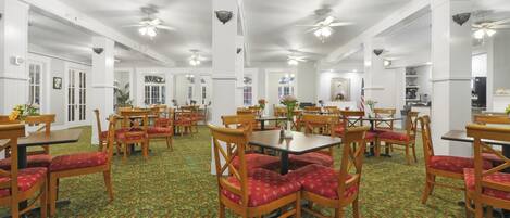 A spacious dining area with multiple tables and chairs, ceiling fans, and a patterned carpet.