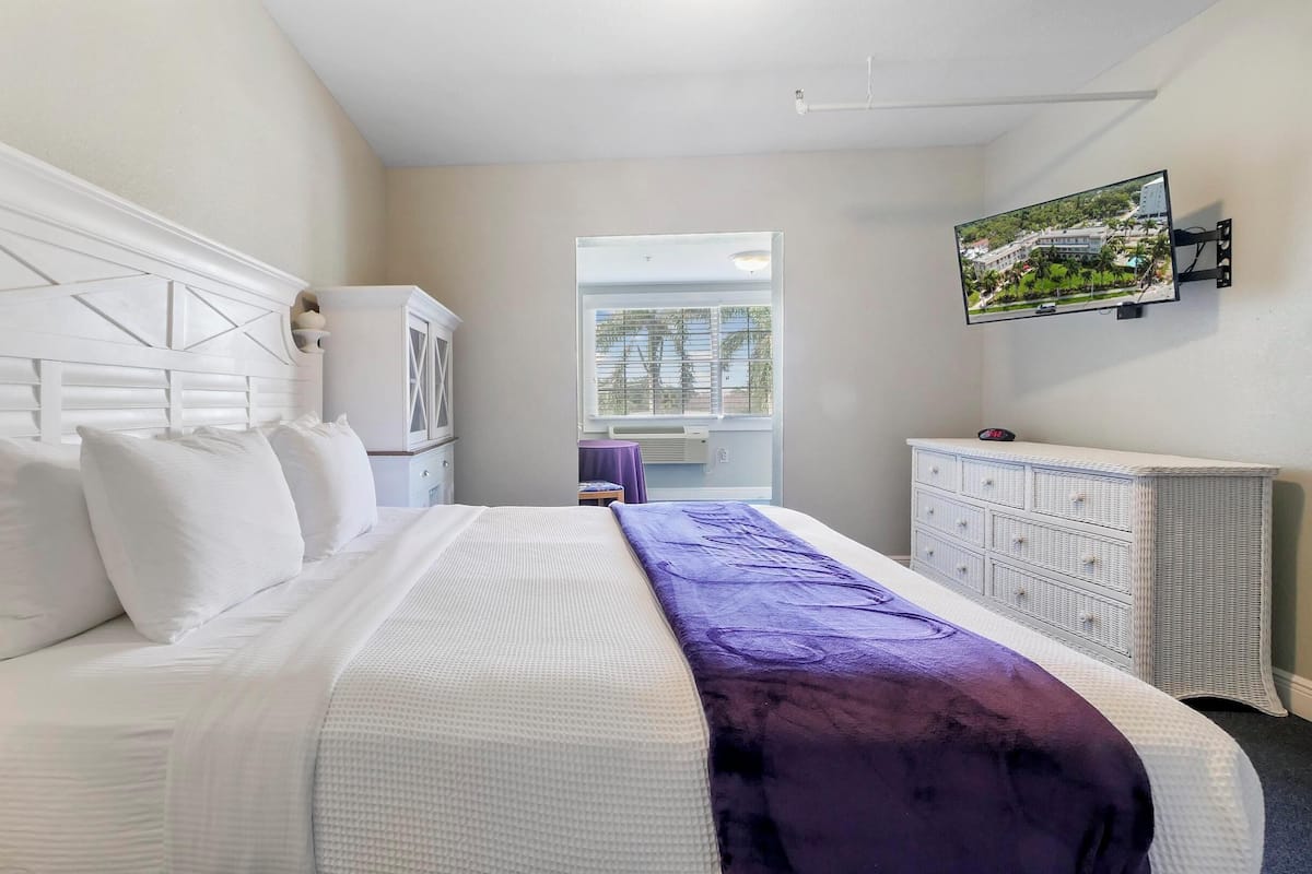 Une chambre d’hôtel avec un grand lit, une tête de lit blanche, une commode, un téléviseur fix é au mur et une fenêtre donnant sur des immeubles.