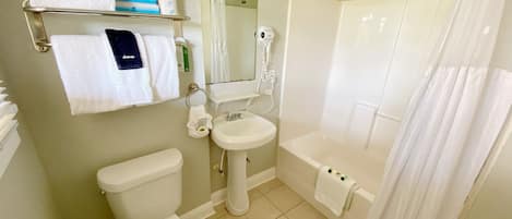 A bathroom with a toilet, sink, and shower. There are towels and toiletries on a shelf.