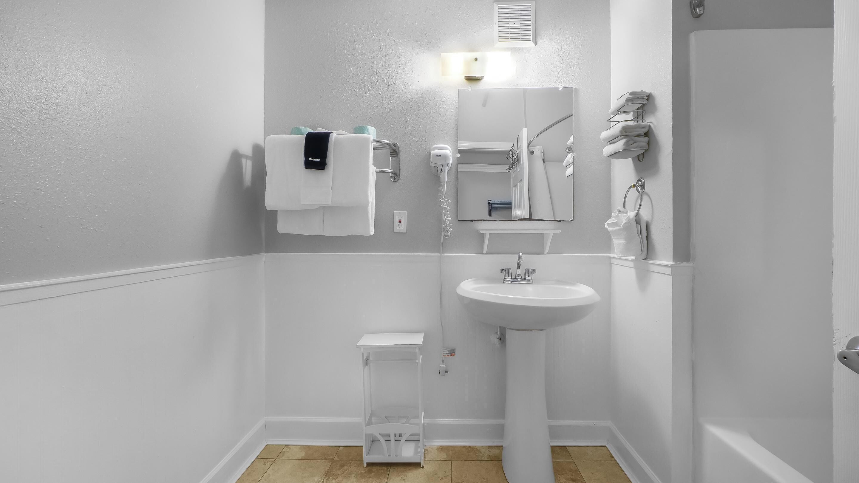 A small, white bathroom with a pedestal sink, a mirror, a towel rack, and a toilet.