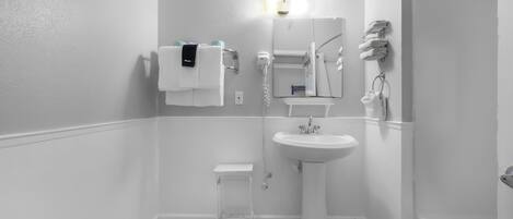 A small, white bathroom with a pedestal sink, a mirror, a towel rack, and a toilet.
