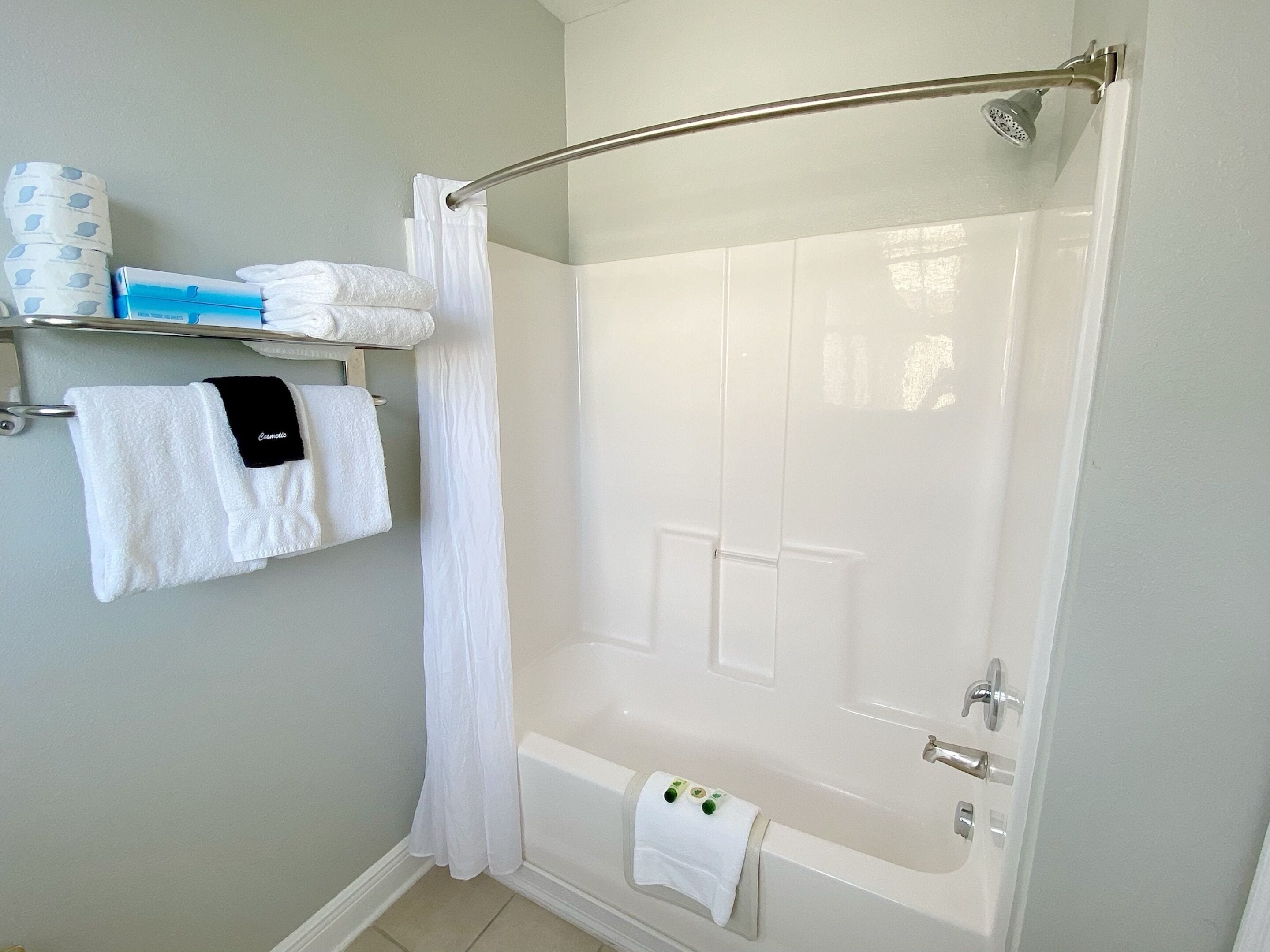 A bathroom with a bathtub, a shower curtain, and a towel rack with multiple towels.