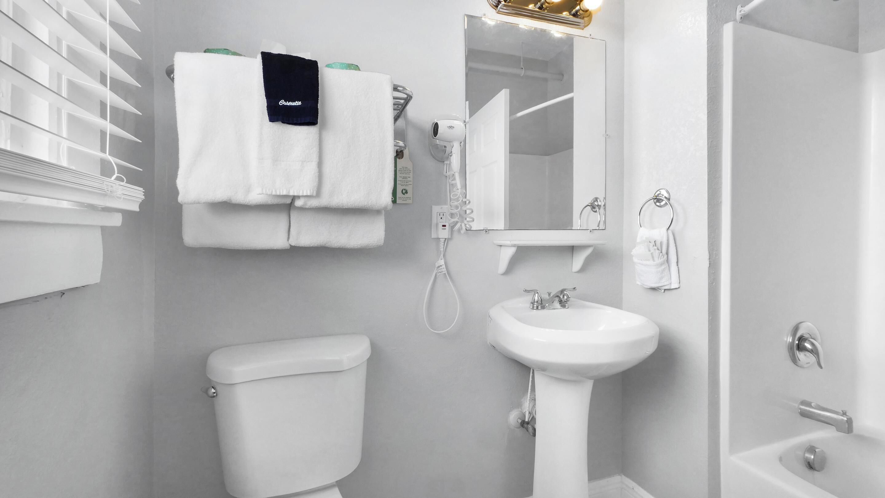 Un baño moderno con inodoro, lavamanos y ducha. Hay toallas blancas colgadas en un perchero y un secador de pelo montado en la pared.