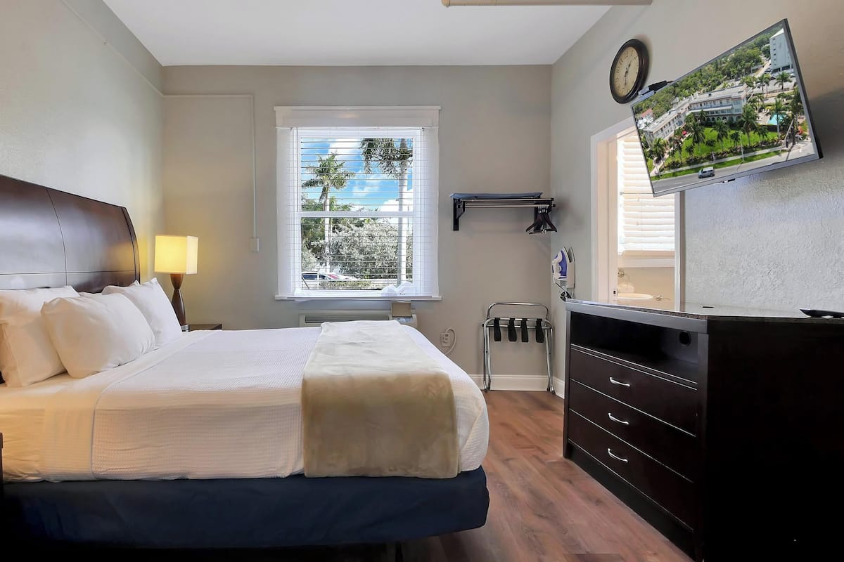 Une chambre d’hôtel équipée d’un lit, d’un bureau, d’une commode, d’une télévision et d’une fenêtre avec des stores.