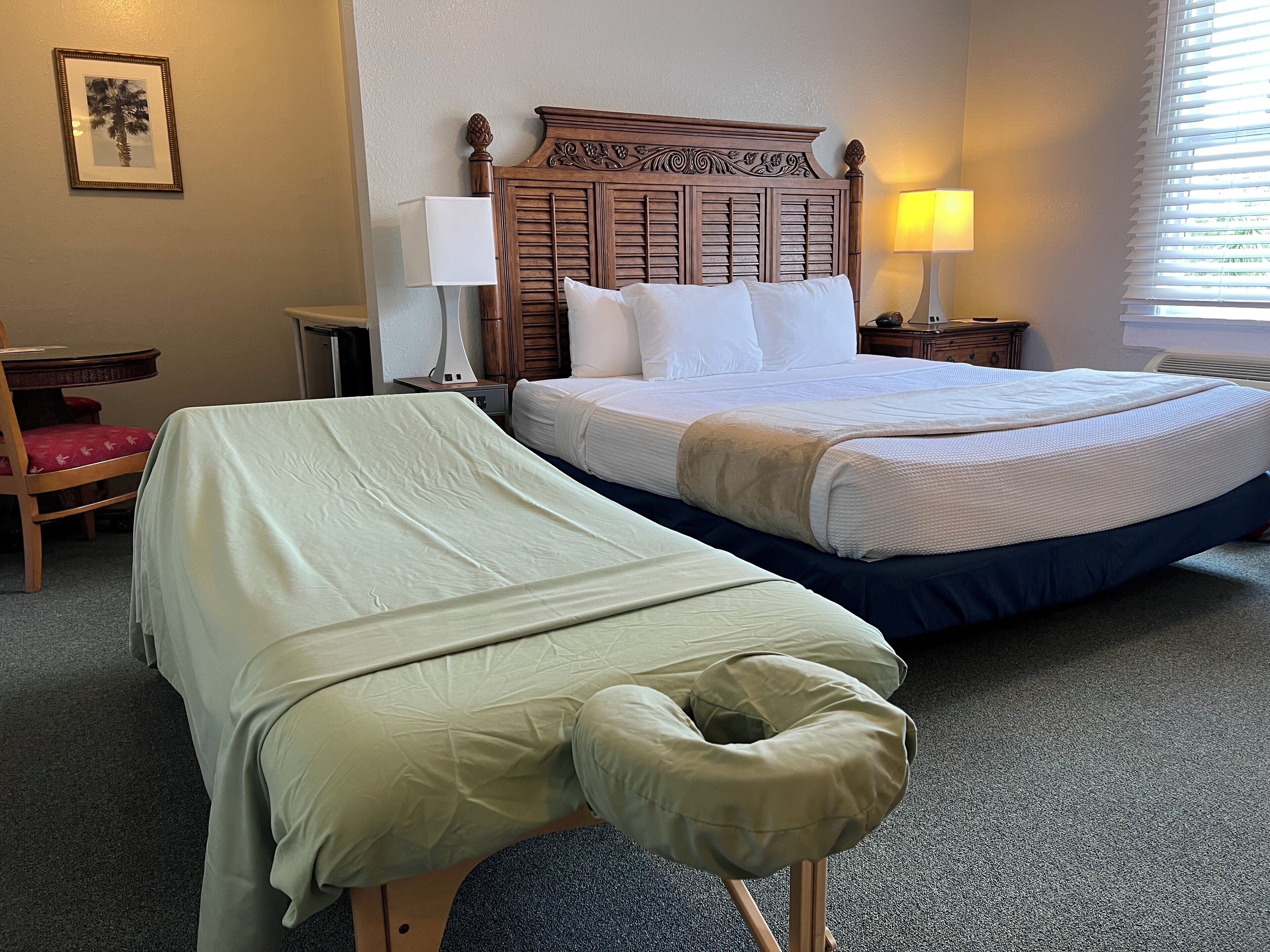 Habitación de hotel con una cama grande, una cama más pequeña, un escritorio con una silla, una lámpara y un cuadro en la pared.