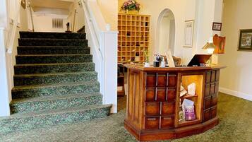 Una escalera con alfombra floral, un mostrador de recepción de madera y un espejo en la pared.