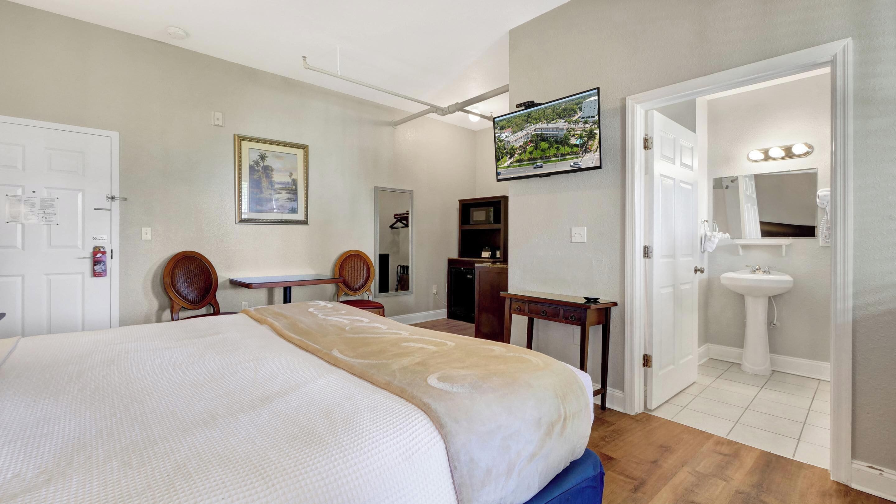 A hotel room with a bed, a desk, a television, a mirror, and a bathroom with a sink and mirror.