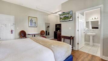 A hotel room with a bed, a desk, a television, a mirror, and a bathroom with a sink and mirror.