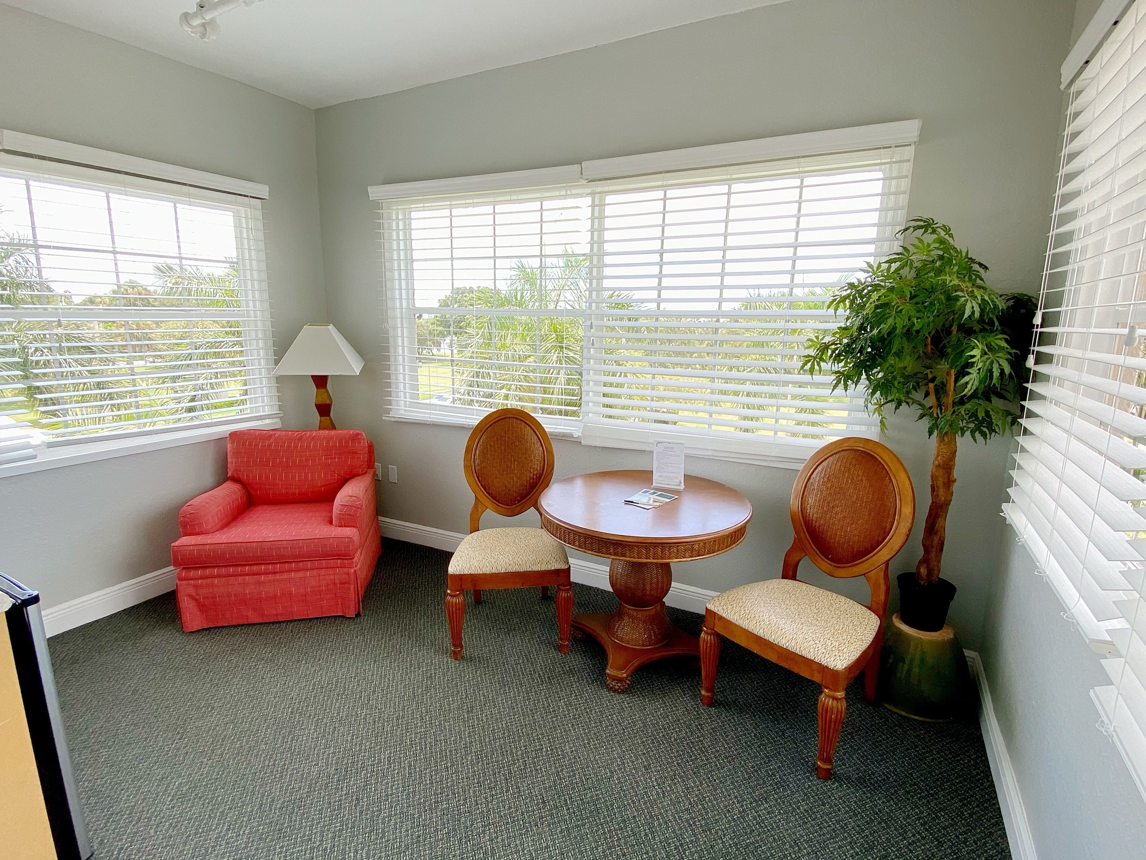 A room with a red armchair, two wicker chairs, a small round table, and a potted plant.