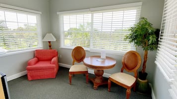 A room with a red armchair, two wicker chairs, a small round table, and a potted plant.
