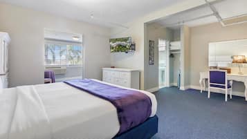 A hotel room with a bed, a desk, a chair, a dresser, a window, and a TV.