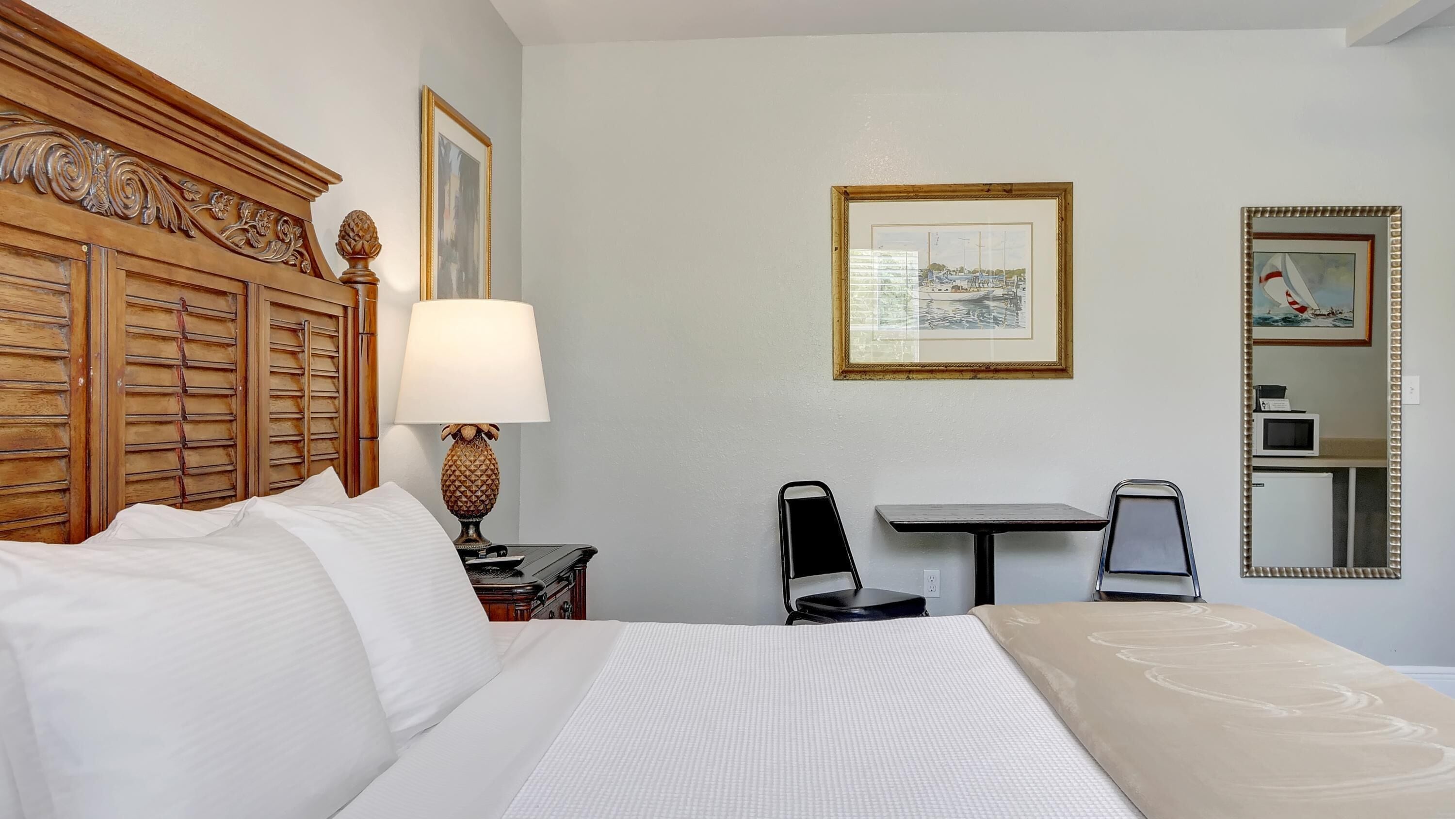 Ein Hotelzimmer mit Bett, Schreibtisch, Stuhl, Lampe und Spiegel.