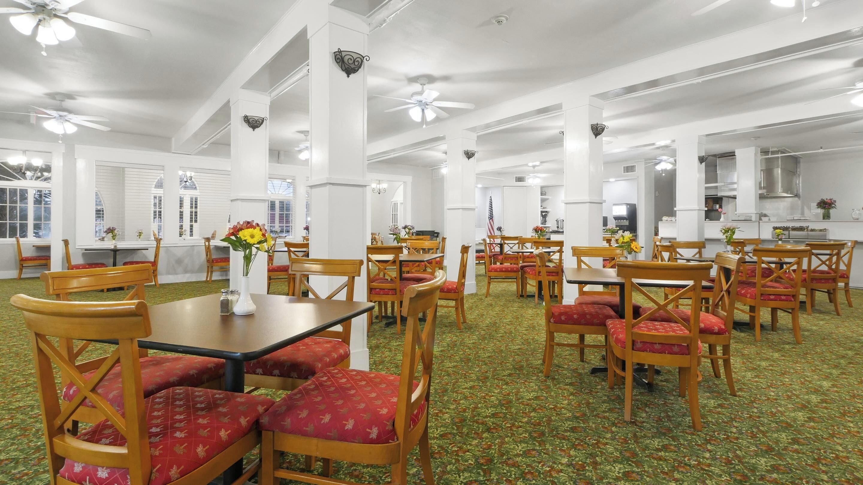 A spacious dining area with high ceilings, multiple tables and chairs, and a green patterned carpet.