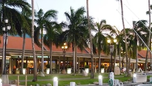 A marina with boats docked, palm trees, and a building with a red roof in the background.