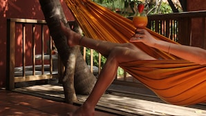 A person relaxing in a hammock outdoors, with a wooden bench and a railing in the background.