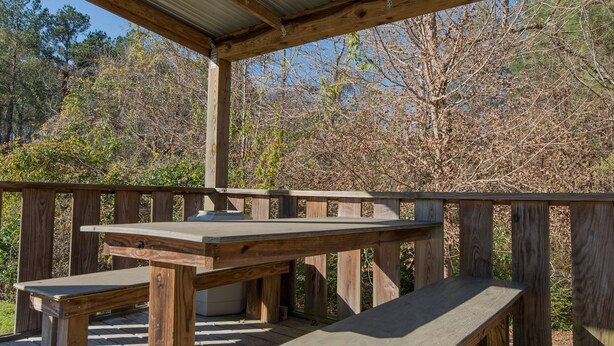 A covered wooden deck with picnic tables and benches, surrounded by trees. - The Stagecoach Inn of Woodville (Woodville)