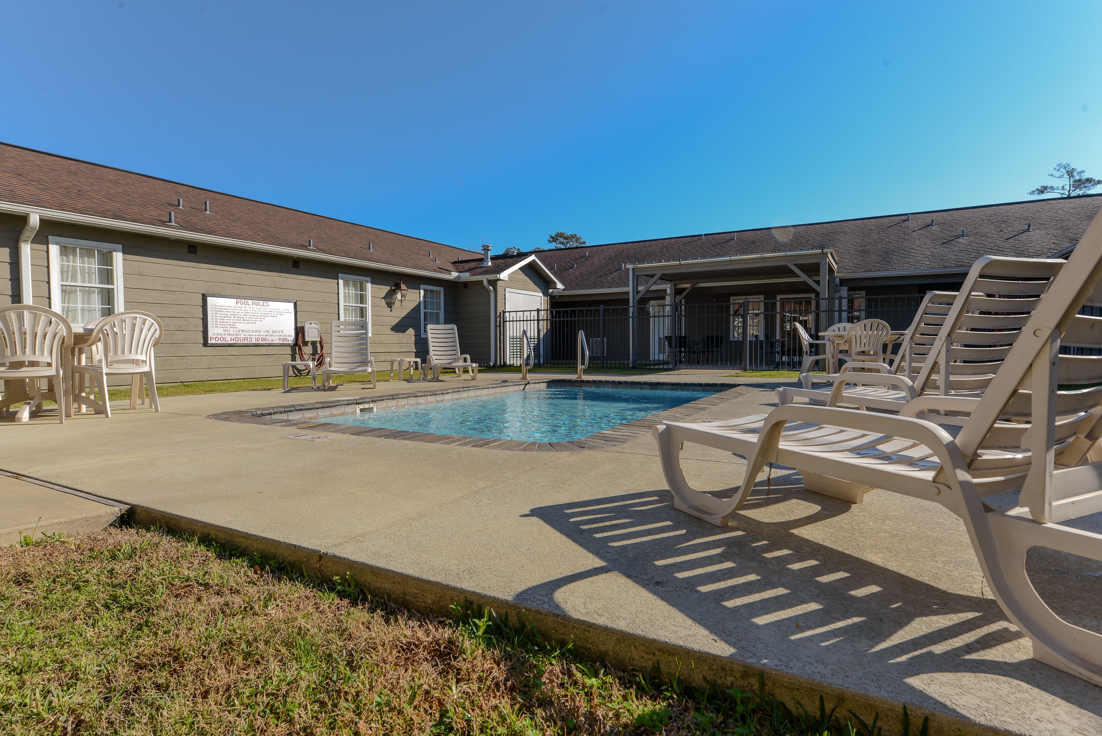 A pool area with lounge chairs, a covered seating area, and a building with a sign.