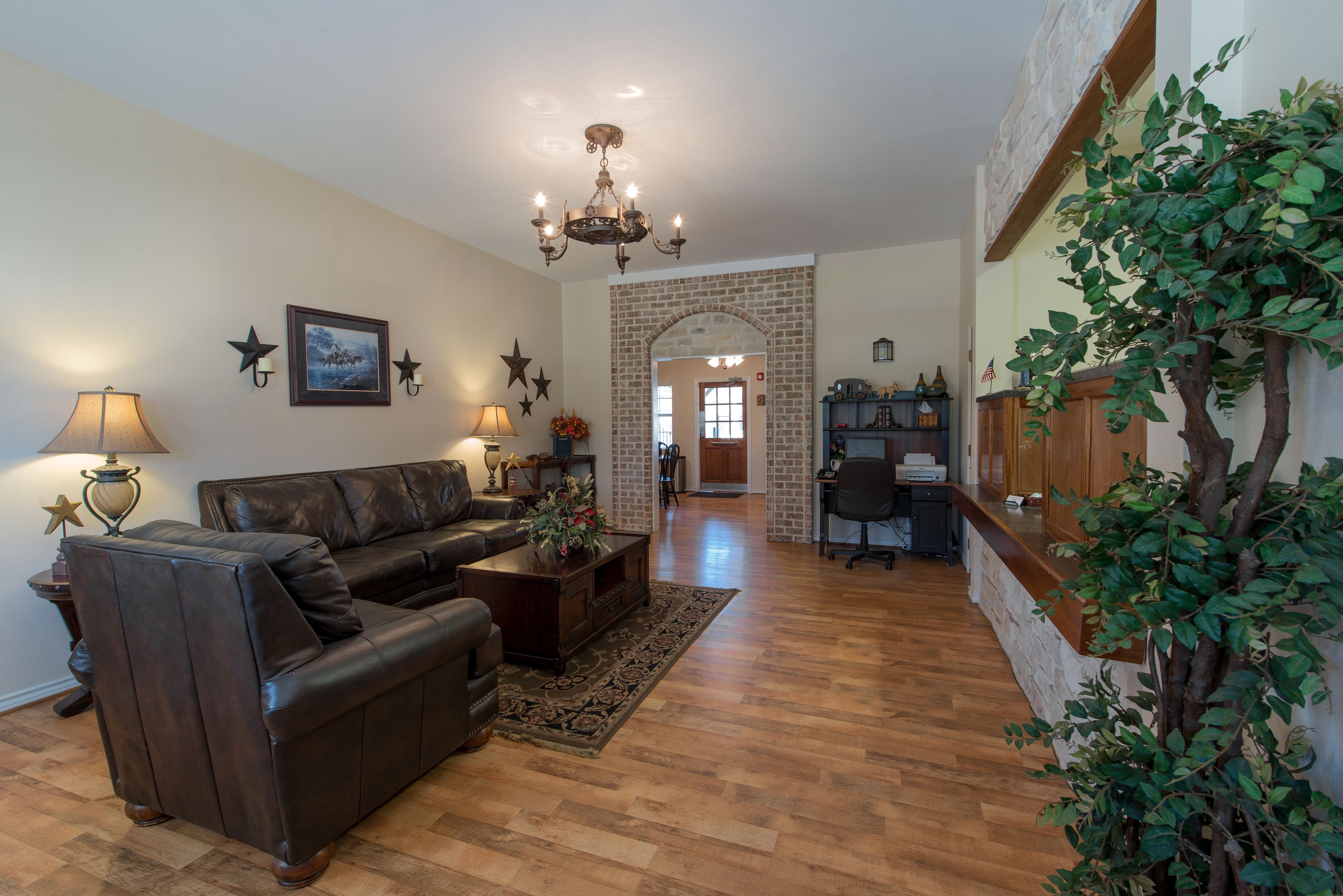 A living room with a leather sofa, a coffee table, and a chandelier. There is a brick fireplace and a wooden cabinet.