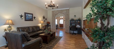 A living room with a leather sofa, a coffee table, and a chandelier. There is a brick fireplace and a wooden cabinet.