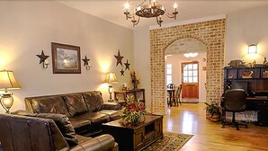A living room with a leather sofa, a coffee table with a floral centerpiece, and a chandelier. There is a brick wall with an archway leading to another room. - The Stagecoach Inn of Woodville (Woodville)