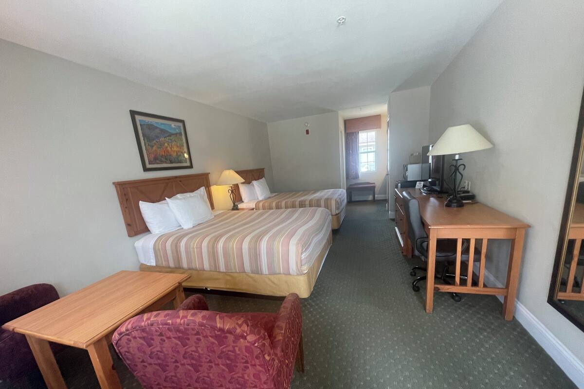 A hotel room with two beds, a desk, a chair, and a small table.