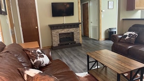 A living room with a leather sofa, a wooden coffee table, a stone fireplace, and a television mounted on the wall. - The Stagecoach Inn of Woodville (Woodville)