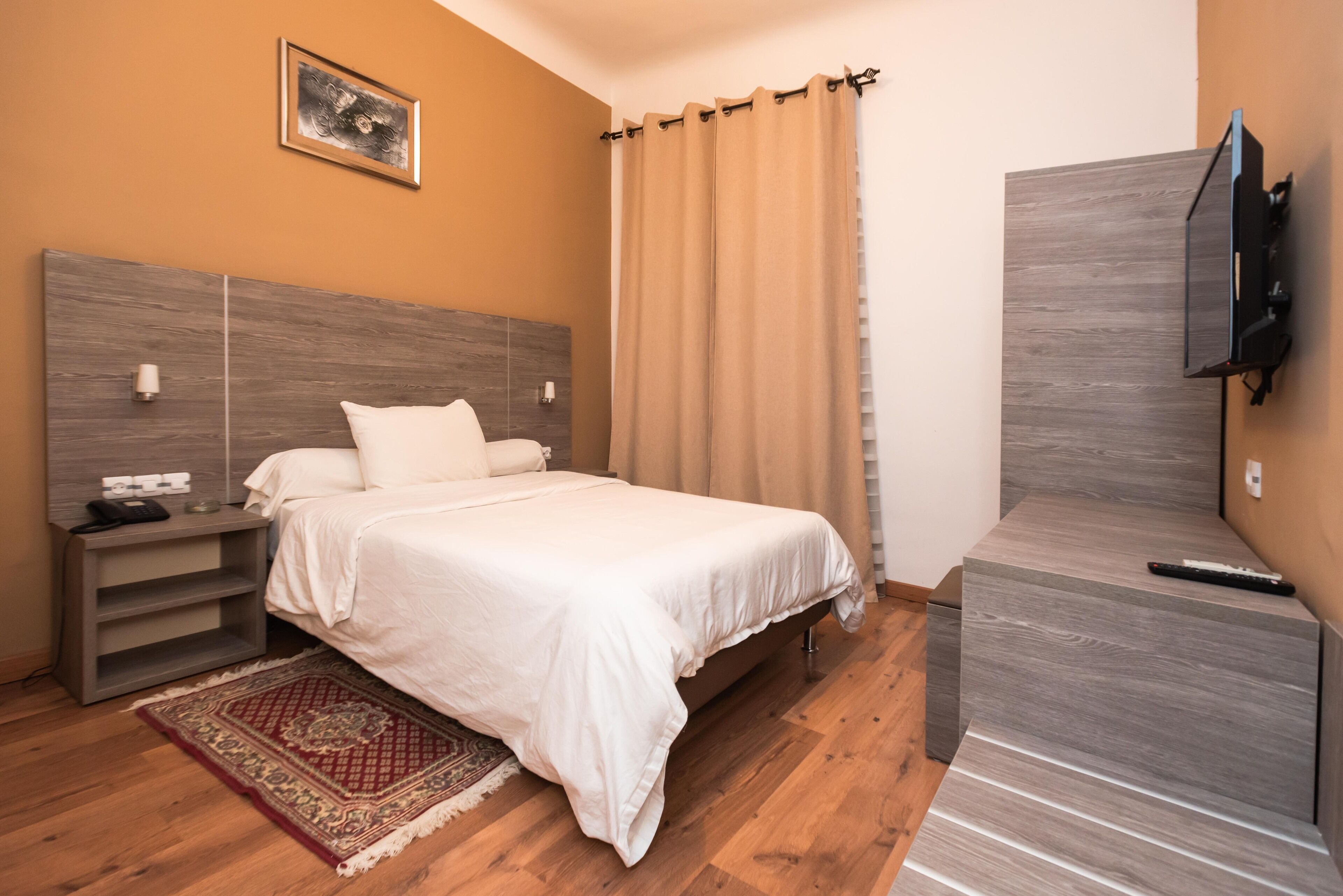 A bedroom with a bed, nightstand, TV, and a wooden floor.