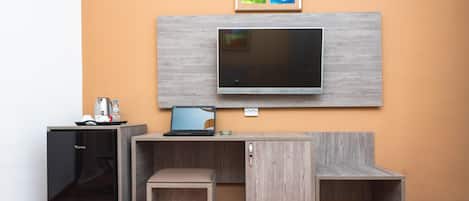 A compact room with a built-in TV, a small fridge, a desk, and a bench.