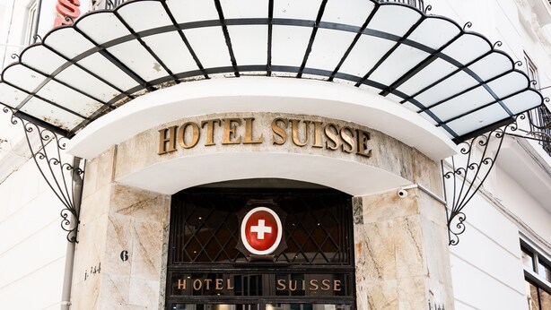 The entrance to Hotel Suisse with a prominent sign, a red cross symbol, and a glass door. - Hôtel Suisse (Algiers)