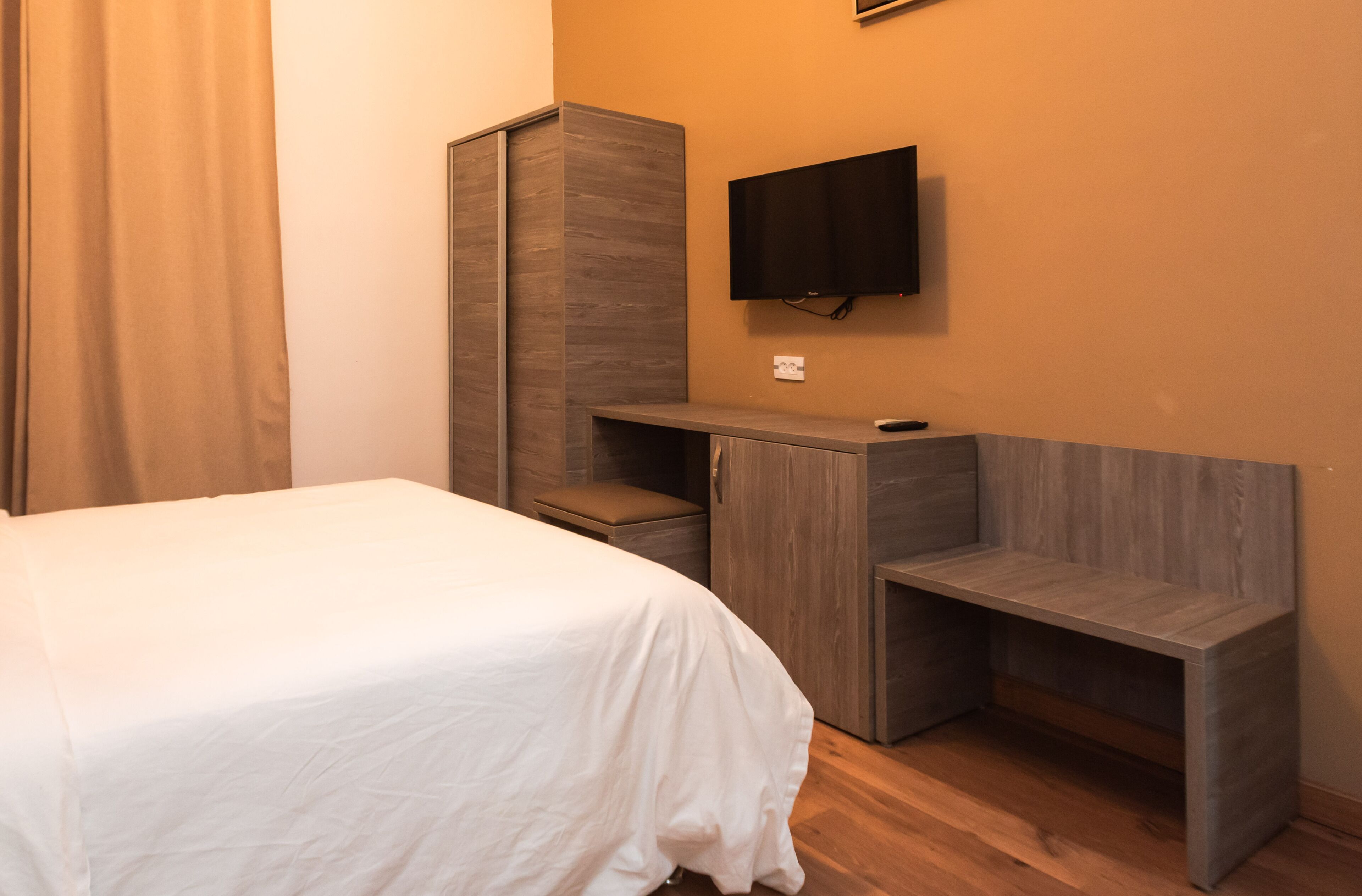 A bedroom with a bed, a desk, and a TV mounted on the wall.