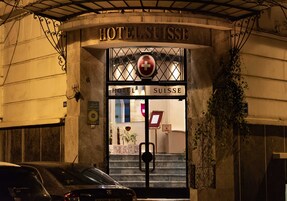 La entrada del Hotel Suisse, con un cartel llamativo, un símbolo de cruz roja y una escalera que lleva a la entrada.