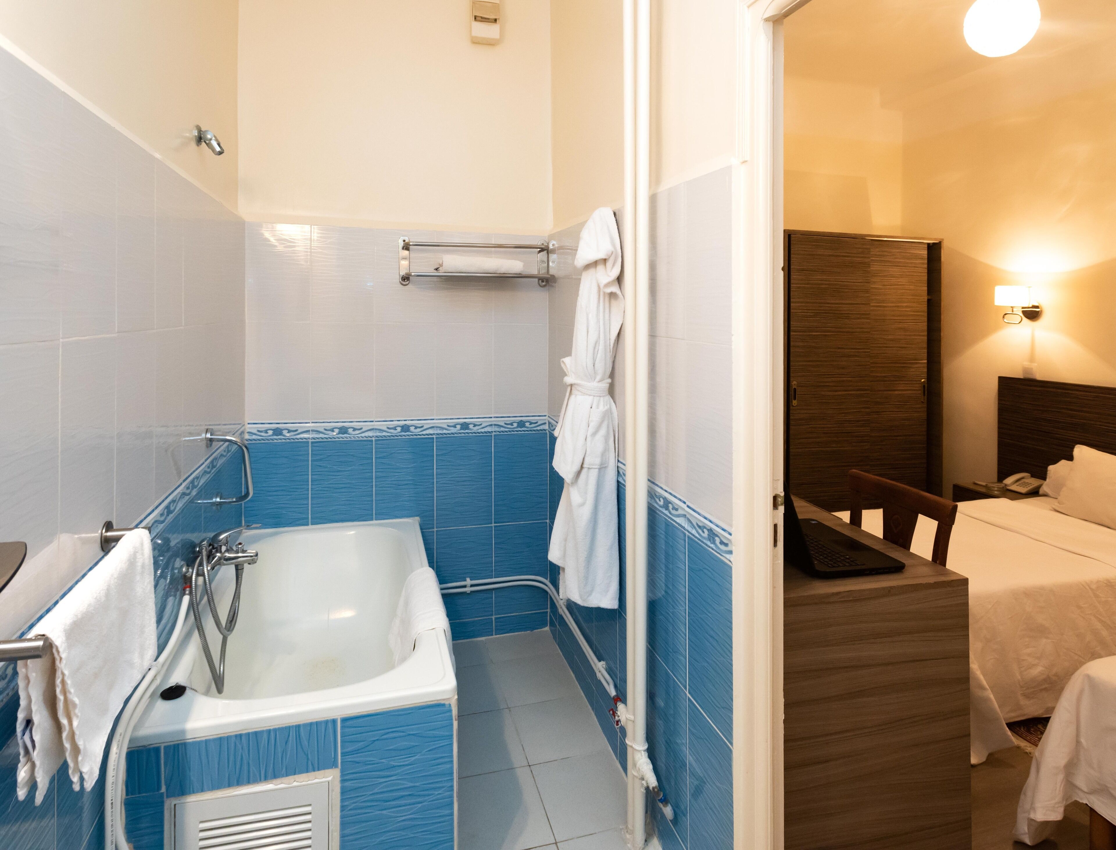 A bathroom with a bathtub, a towel rack, and a shower. There is a wooden headboard in the adjacent room.