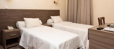 A hotel room with two beds, a desk, a chair, a telephone, and a lamp on the wall.