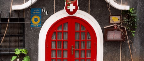 Una puerta roja con un arco blanco, una bandera suiza y un cartel con texto en árabe.