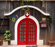 Una puerta roja con un arco blanco, una bandera suiza y un cartel con texto en árabe.