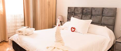 Una cama bien hecha con un cojín con forma de corazón, una bata sobre la cama y un armario de madera en una habitación de hotel.